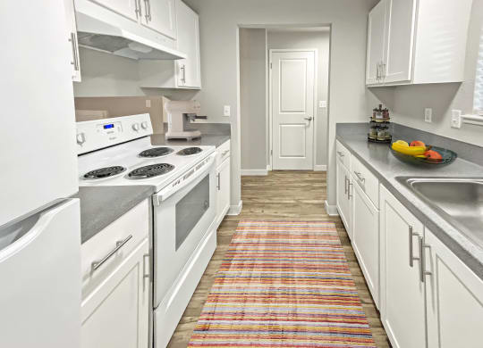 Double galley kitchen, wood-like floors, full-size fridge, top and bottom cabinets, oven, stovetop, and sink.at Quilceda Gardens, Marysville, 98270