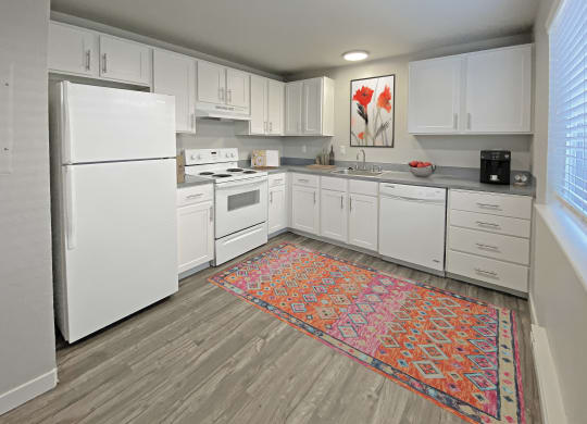 L-shaped kitchen with top and bottom cabinet storage, gray countertops, white appliances, and a large window on the right wall.at Quilceda Gardens, Washington