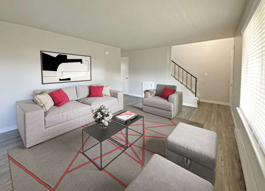 Living room with stairs on far wall and oversized window on the right wall. Staged with couch, chair, 2 ottomans, rug, and table.at Quilceda Gardens, Marysville, WA 98270