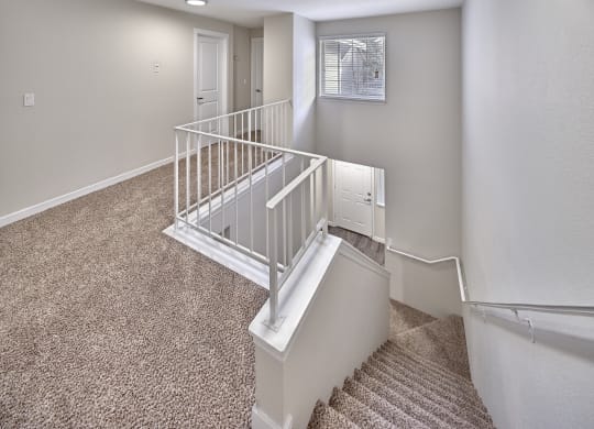 Carpeted stairs with white railings look down to the first floor. Above the stairs is a large window at Arterra Apartments, Washington