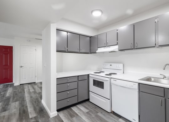 an open kitchen at Summit Apartments with grey cabinets and faux wood flooring, white countertop and white appliances.