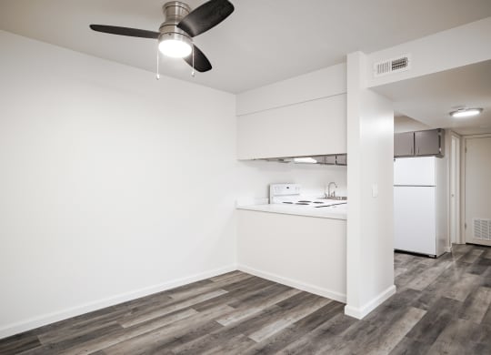 an empty living room with a kitchen and a ceiling fan