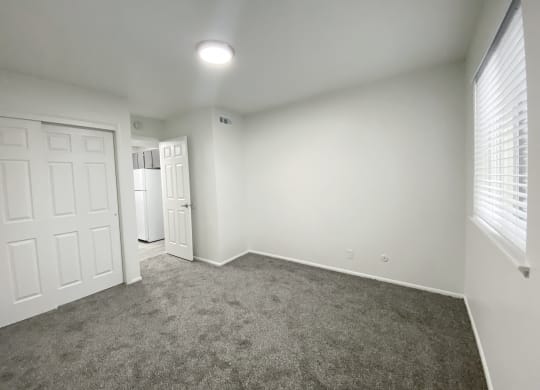Bedroom with large sliding door closet, oversized window with white blinds on right, and door to hallway in back left corner at Summit, Pocatello, ID 83201