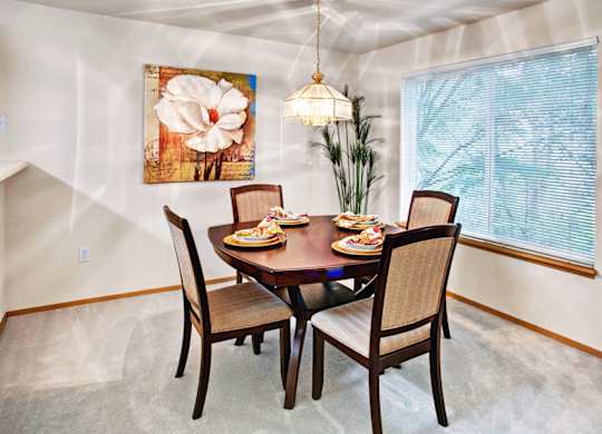 A dining room with a table set for two and a large painting on the wall.