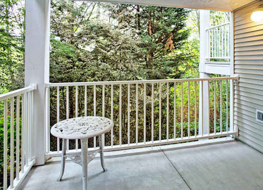 A white table with a circular top is on a porch with a white railing.