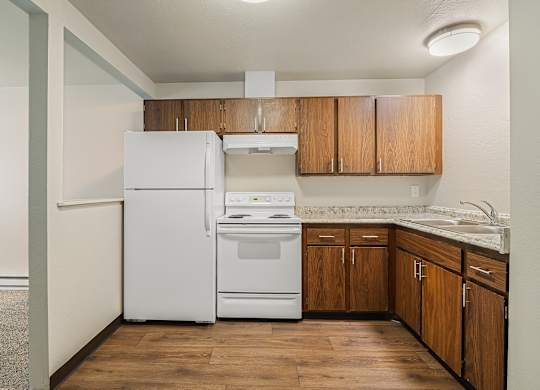Apartment kitchen with wood cabinets, white appliances and functional layout at The Lakes Apartments in Moses Lake WA