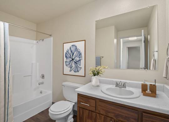 White bathroom with single-sink vanity, toilet, and large mirror in a 2 bed 1 bath apartment at the Lakes in Moses Lake Apartments