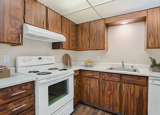 Kitchen with warm wood cabinets, white electric range, and ample counter space at The Lakes Apartments