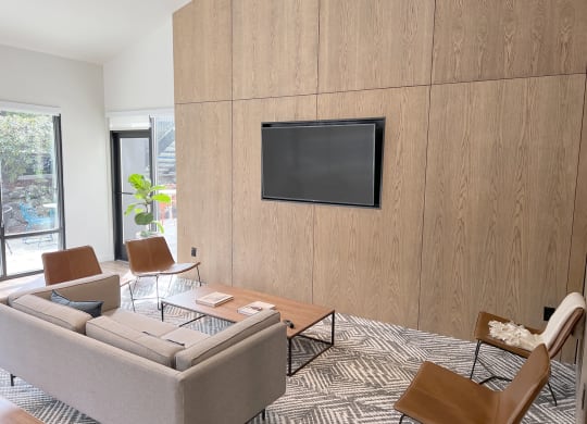 Clubhouse with floor to ceiling windows, a large flat-screen TV, a couch, 4 chairs, a coffee table, rug. The patio is visible from the clubhouse at University Glen, University Place