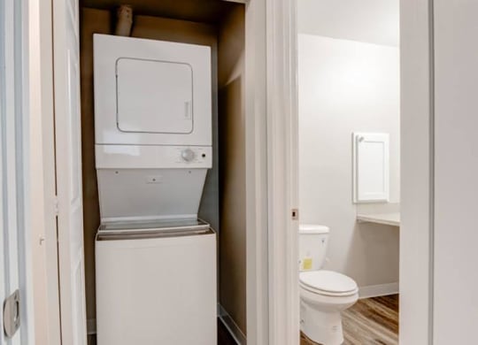 A laundry closet with a white stacked washer and dryer and a door to the bathroom on the right. at Pointe East, Washington, 98424