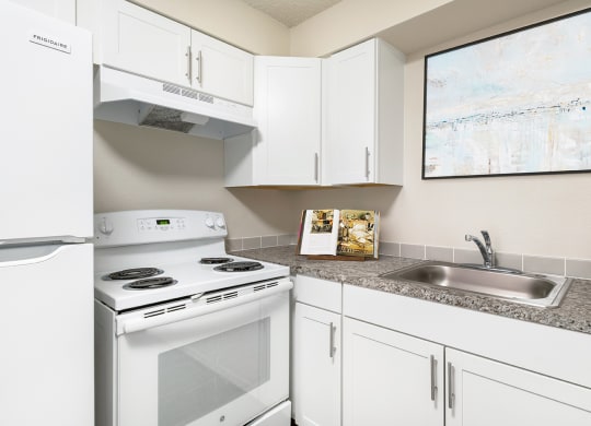 Corner of a kitchen with custom white cabinets, spacious countertops, a stainless steel sink, oven, stovetop and hood range, and full-size fridge.at Wildflower, Washington