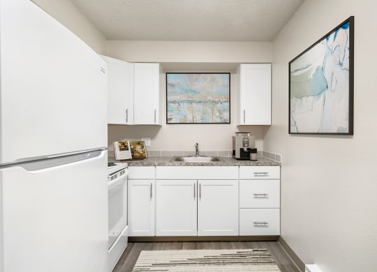 L-shaped kitchen with a full-size fridge, oven, stove top, sink, top and bottom cabinets, and wood-like flooring.at Wildflower, Kennewick, WA