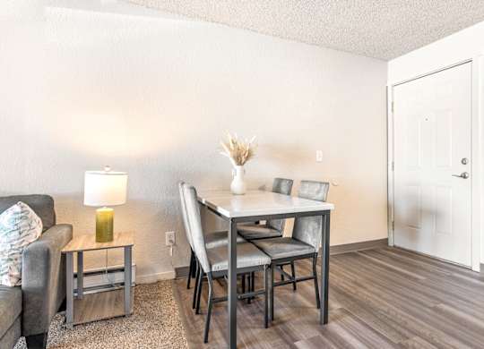 A dining room with a grey table and chairs A bedroom with a bed, nightstand, and window at Wildflower Apartments, Kennewick, WA 99336..