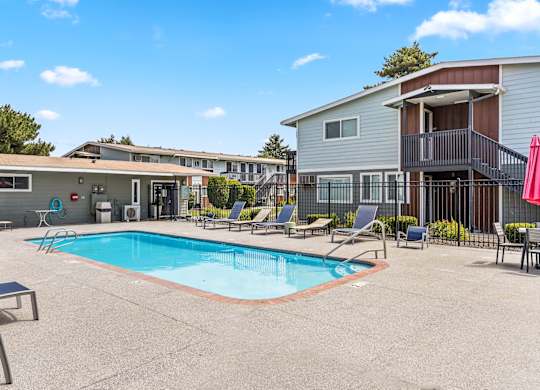 A swimming pool surrounded by lounge chairs and a building in the background t Wildflower Apartments in Kennewick, WA..