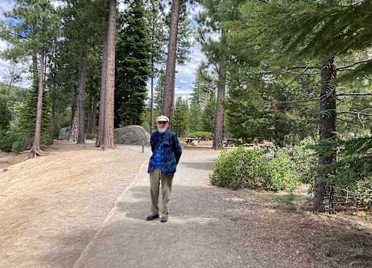 Resident walking through tree lined outdoor pathway at Hilltop Commons Senior Living Apartments, Grass Valley, 95945