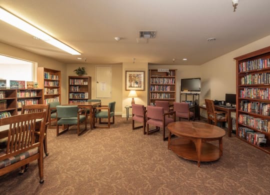a library with tables and chairs and shelves of books at Hilltop Commons Senior Living, Grass Valley, CA