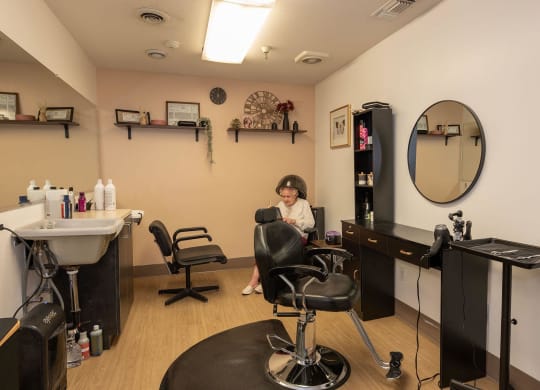 a woman sitting in a salon chair in front of a mirror at Hilltop Commons Senior Living, California