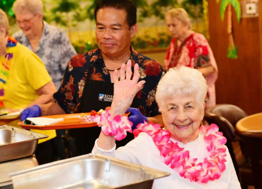 an older woman in a wheelchair gives a high five to a group of older people at River Commons Senior Living, California