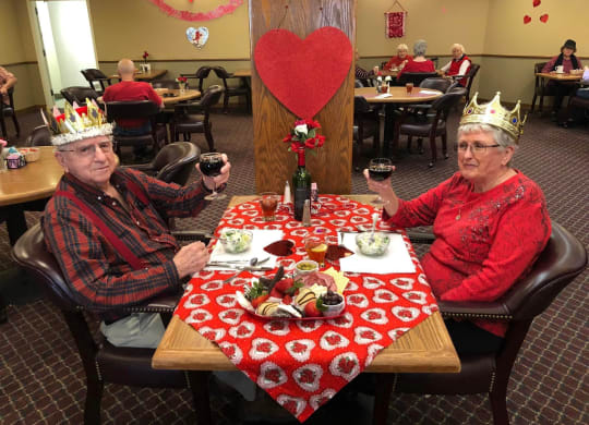 two women sitting at a table wearing crowns and holding wine glasses at River Commons Senior Living, Redding, 96002