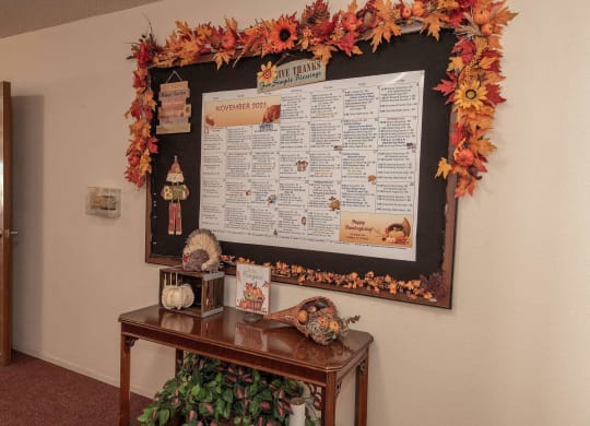 a bulletin board on a wall with fall leaves and decorations on a table at Roseville Commons Senior Living, Roseville, CA