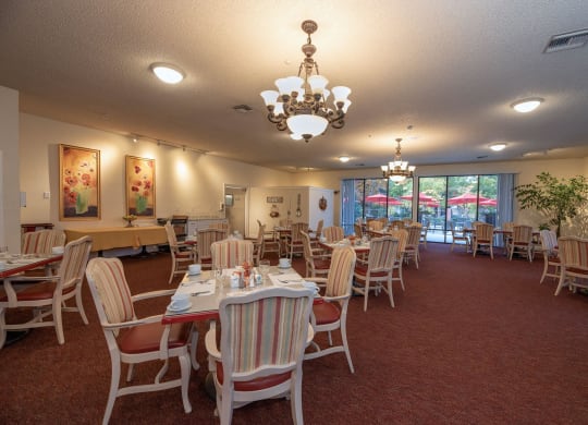 a dining room with tables and chairs and a chandelier at Roseville Commons Senior Living, California, 95678