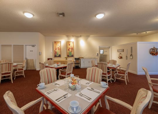 a dining room with tables and chairs and a kitchen at Roseville Commons Senior Living, California