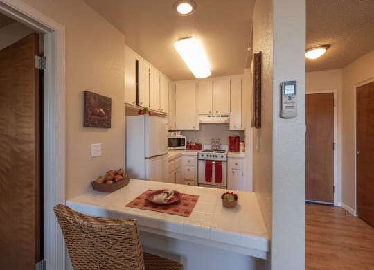 a kitchen with white cabinets and a table with a bowl of fruit at Roseville Commons Senior Living, Roseville, 95678