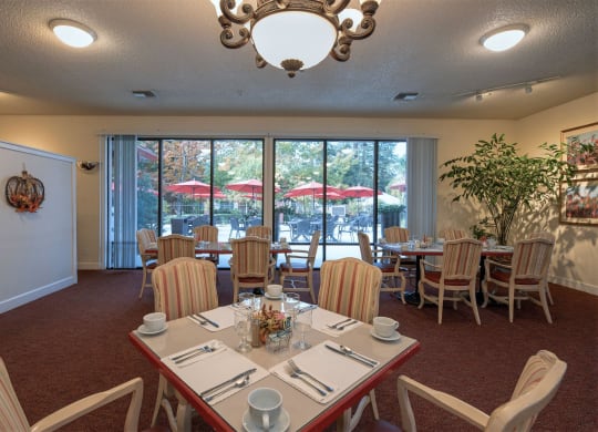 a dining room with tables and chairs and a large window at Roseville Commons Senior Living, Roseville, CA