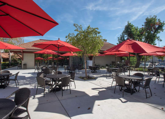 an outdoor patio with tables and red umbrellas at Roseville Commons Senior Living, Roseville
