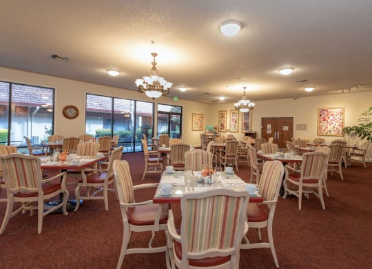 a dining room with tables and chairs and a chandelier at Roseville Commons Senior Living, California, 95678