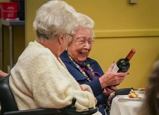 two elderly women sitting at a table with a bottle of wine at Winding Commons Senior Living, Carmichael, 95608