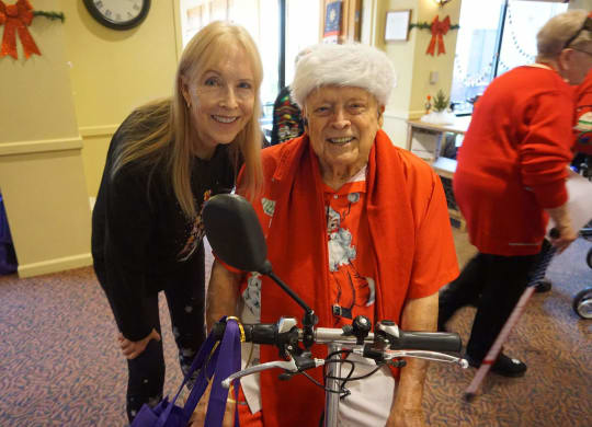 a woman is standing next to an older woman on a bike at Winding Commons Senior Living, Carmichael, CA