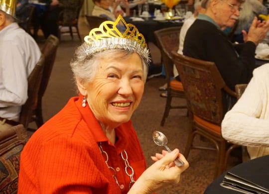 a woman in a crown sitting at a table with a spoon at Winding Commons Senior Living, Carmichael, 95608
