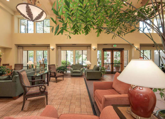 a large lobby with couches and chairs and a large tree in the center at Winding Commons Senior Living, Carmichael, 95608