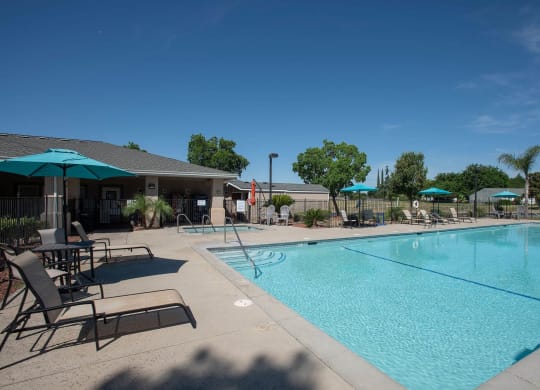 a swimming pool with chairs and umbrellas next to a building at Castle Vista Senior Duplex Community, Atwater, California