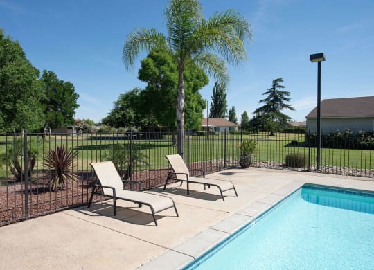 a swimming pool with two lounge chairs next to a fence at Castle Vista Senior Duplex Community, Atwater