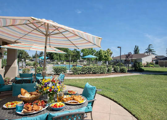 Outdoor dining area with umbrella and pool view at Castle Vista Senior Duplex Community Apartments, Atwater, 95301