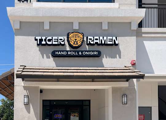 A white building with a black and gold sign that says Tiger Ramen at Discovery at Craig Ranch, McKinney, TX