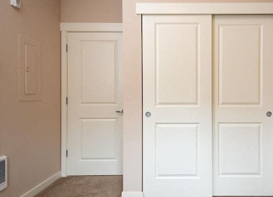 a closet with two white doors and a door to a hallway