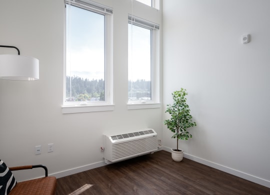 a living room with three windows, an air conditioner,  and a plant