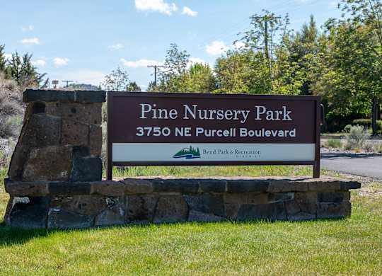 A sign for Pine Nursery Park stands in front of a grassy area.