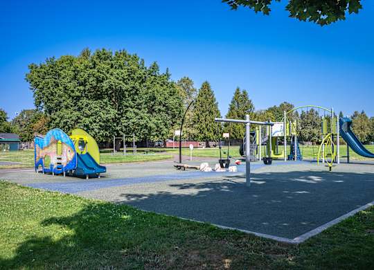 A playground with a yellow and blue slide, a green swing set, and a red and white seesaw.
