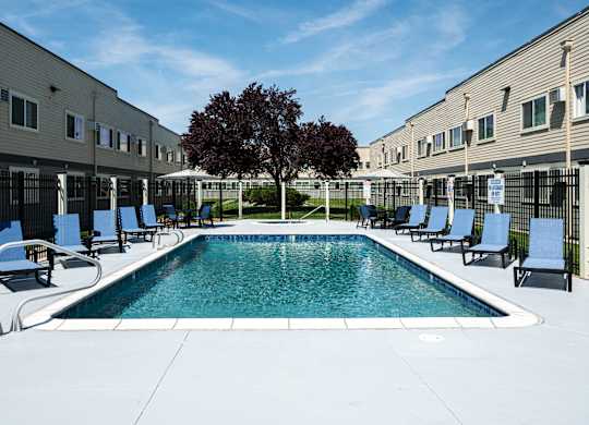 A swimming pool surrounded by chairs and a tree in a sunny courtyard.
