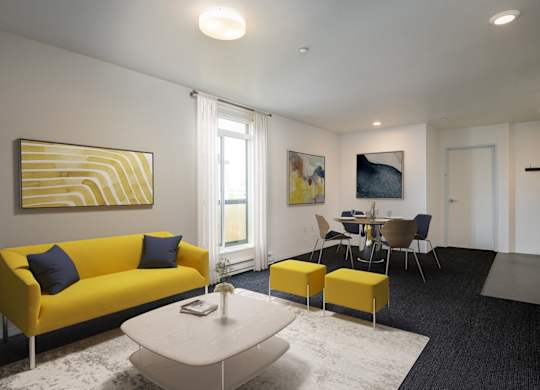 A living room with a yellow couch and a painting on the wall.