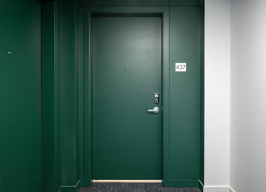A green door with a silver handle and a number 437 on the wall.