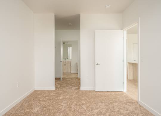 A white room with a carpeted floor and a doorway leading to another room.