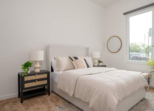 A bedroom with a bed, nightstand, and a plant.