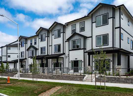 A row of modern townhouses with a sidewalk and a street lamp.