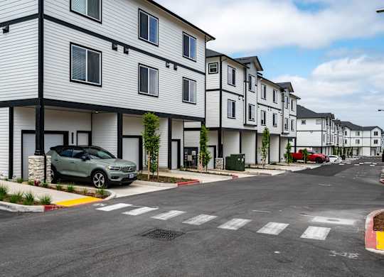 A row of white houses with a green car parked in front of the first one.