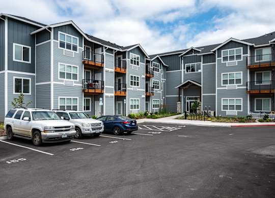 A parking lot in front of a grey apartment building with two cars parked.